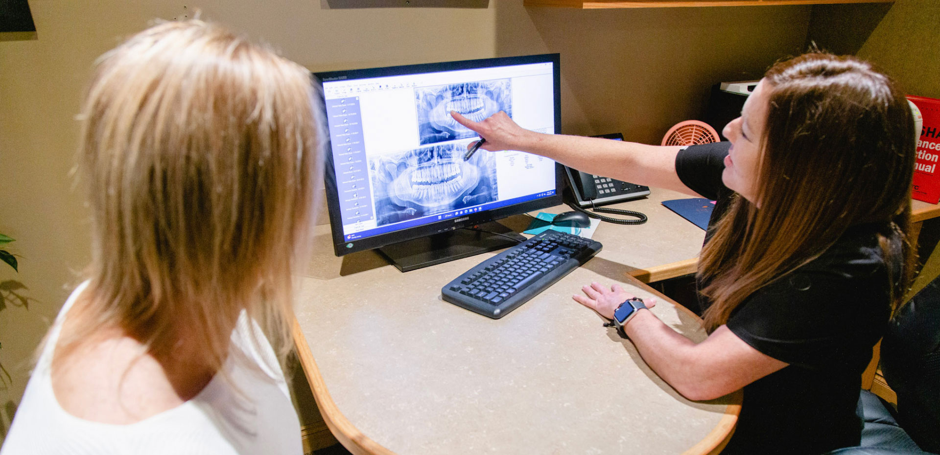 patient with dental assistant pointing to dental x-rays on computer monitor